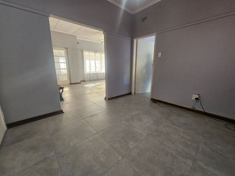An empty living area featuring neutral grey floor tiles, coved cornicing, and direct access to an adjoining room.
