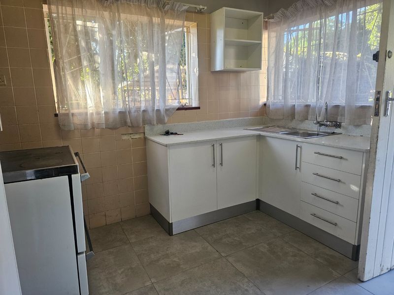 A functional kitchen featuring white cabinetry, stone countertops, a stainless steel sink, and tiled splashbacks, offering a clean and practical workspace.