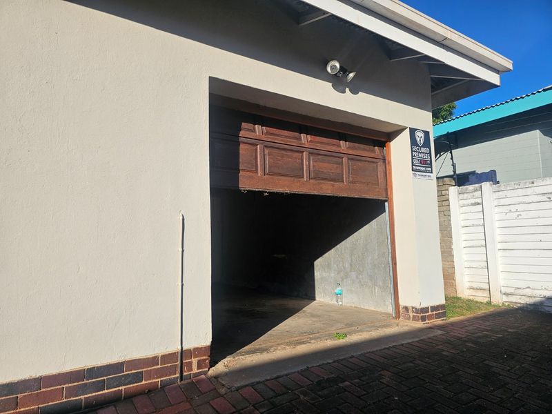 A single garage with a wooden sectional door, security lighting, and paved driveway access.