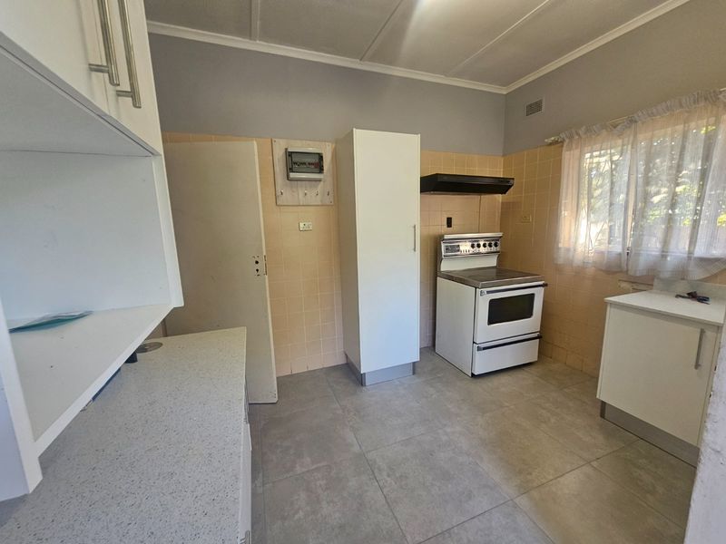 A functional kitchen featuring tiled flooring, built-in cabinetry, and a freestanding stove with an extractor fan, offering potential for modernization and cosmetic updates.