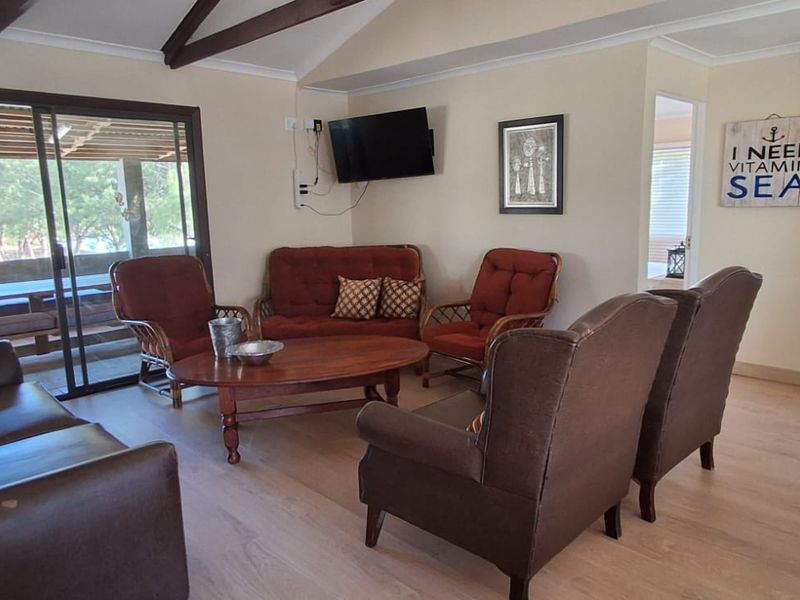 A living room featuring vaulted ceilings with exposed timber beams, laminate flooring, and a sliding glass door providing access to an outdoor patio area.