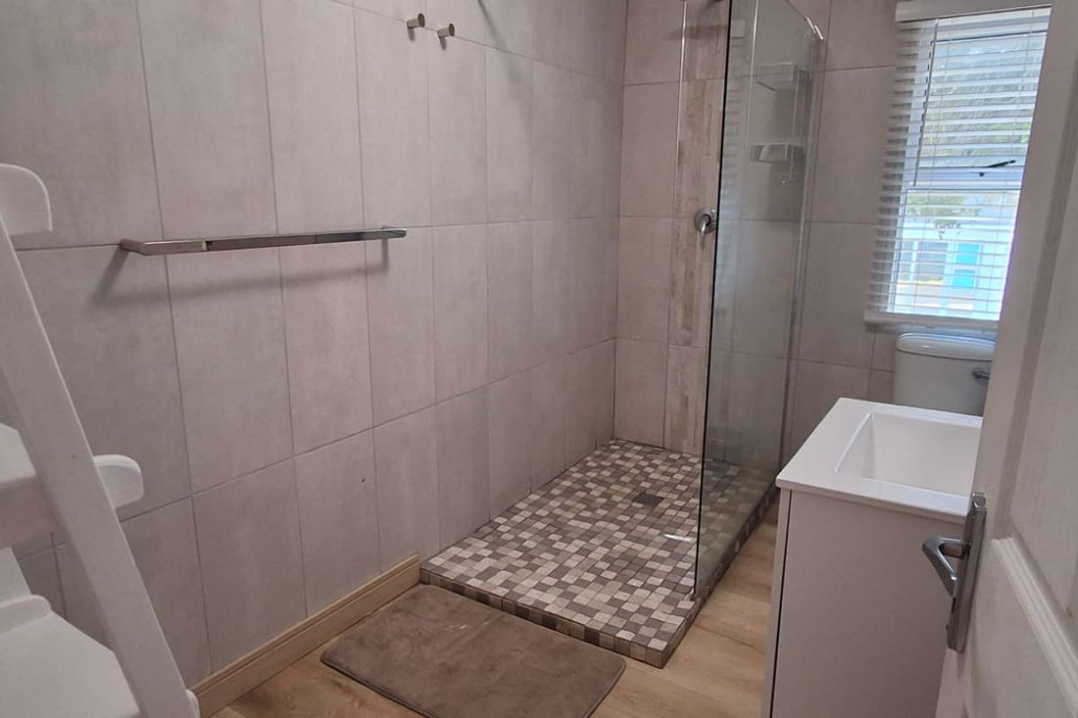 A modern bathroom featuring a glass-enclosed shower with mosaic tiling, a vanity basin, and a toilet, finished with neutral wall tiles.