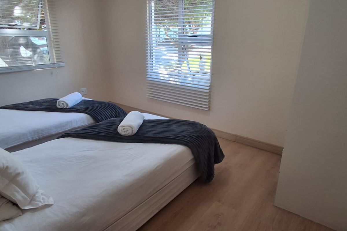 A functional bedroom featuring laminate flooring and venetian blinds, providing a neutral space with natural light.