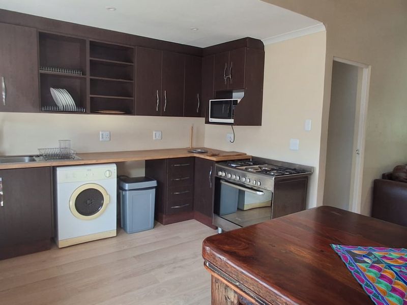 Open plan kitchen featuring dark wood cabinetry, stainless steel appliances, and laminate flooring, seamlessly flowing into the adjacent living area.