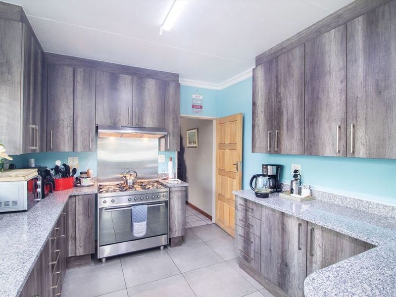 A functional kitchen featuring modern grey wood-grain cabinetry, granite countertops, and a stainless steel gas stove with an integrated extractor fan.