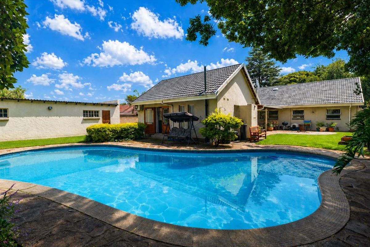 A well-maintained backyard featuring a large swimming pool with a stone-tiled surround, set against the rear elevation of the house.