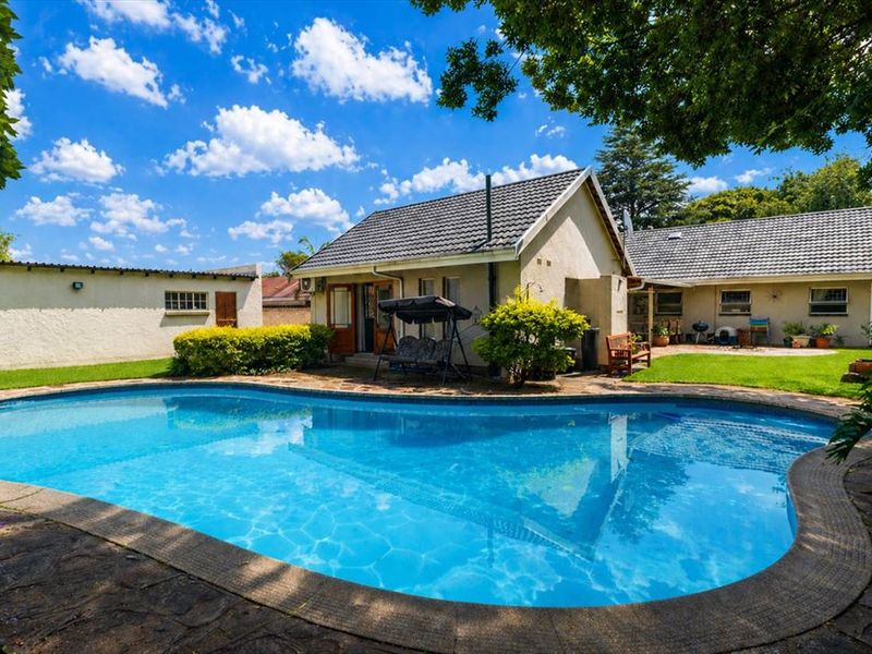 A well-maintained backyard featuring a large swimming pool with a stone-tiled surround, set against the rear elevation of the house.