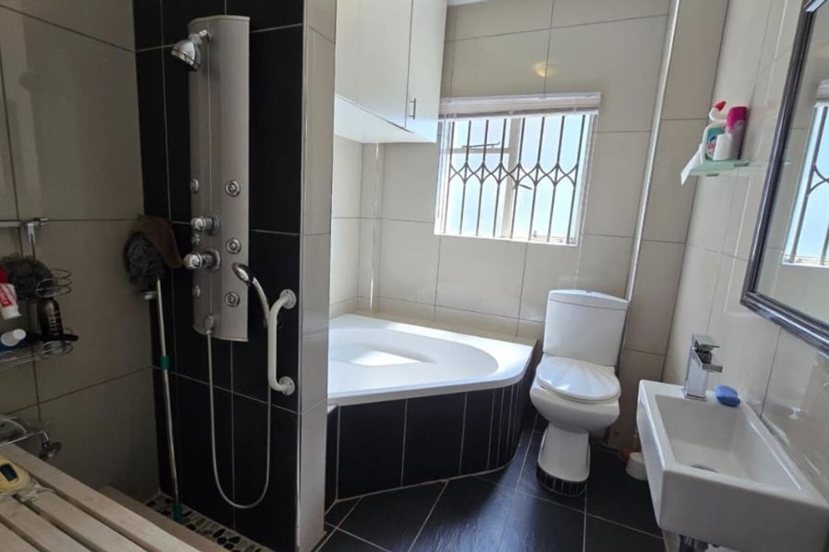 Modern bathroom featuring a corner bathtub, a contemporary shower panel, wall-mounted basin, and tiled finishes throughout.