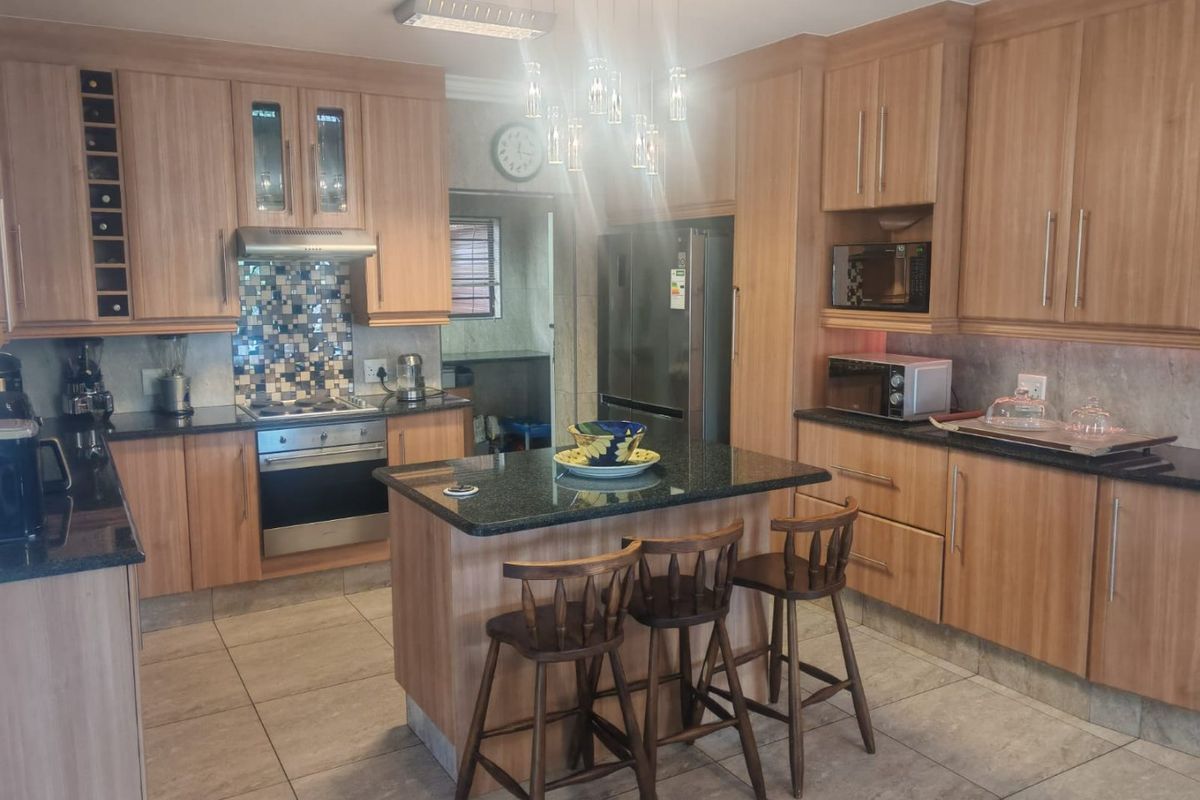 A well-maintained kitchen featuring light wood cabinetry, granite countertops, a central island with seating, and a mosaic tile backsplash.