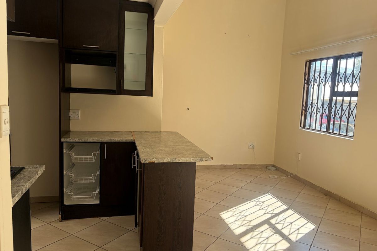 An empty kitchen area featuring dark wood cabinetry, laminate countertops, tiled flooring, and a window fitted with a security gate.