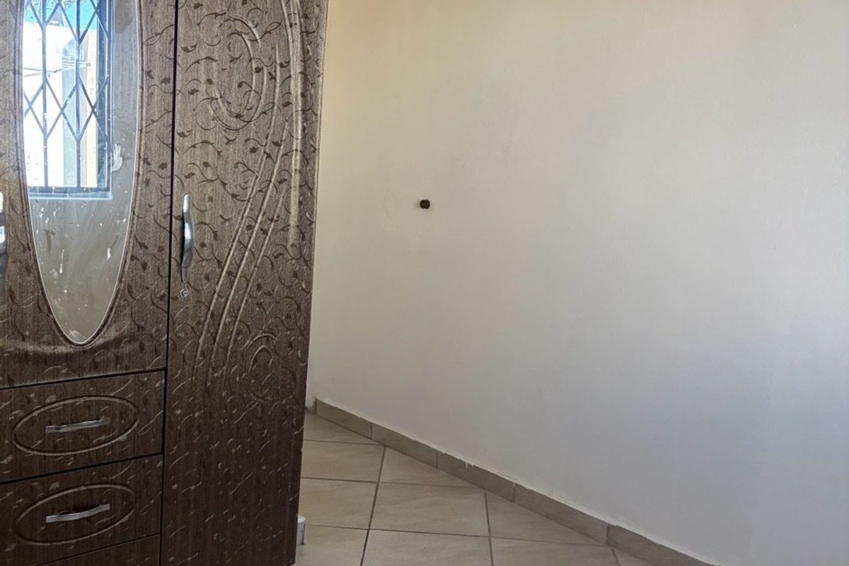 A bedroom featuring tiled flooring and a window with security bars.