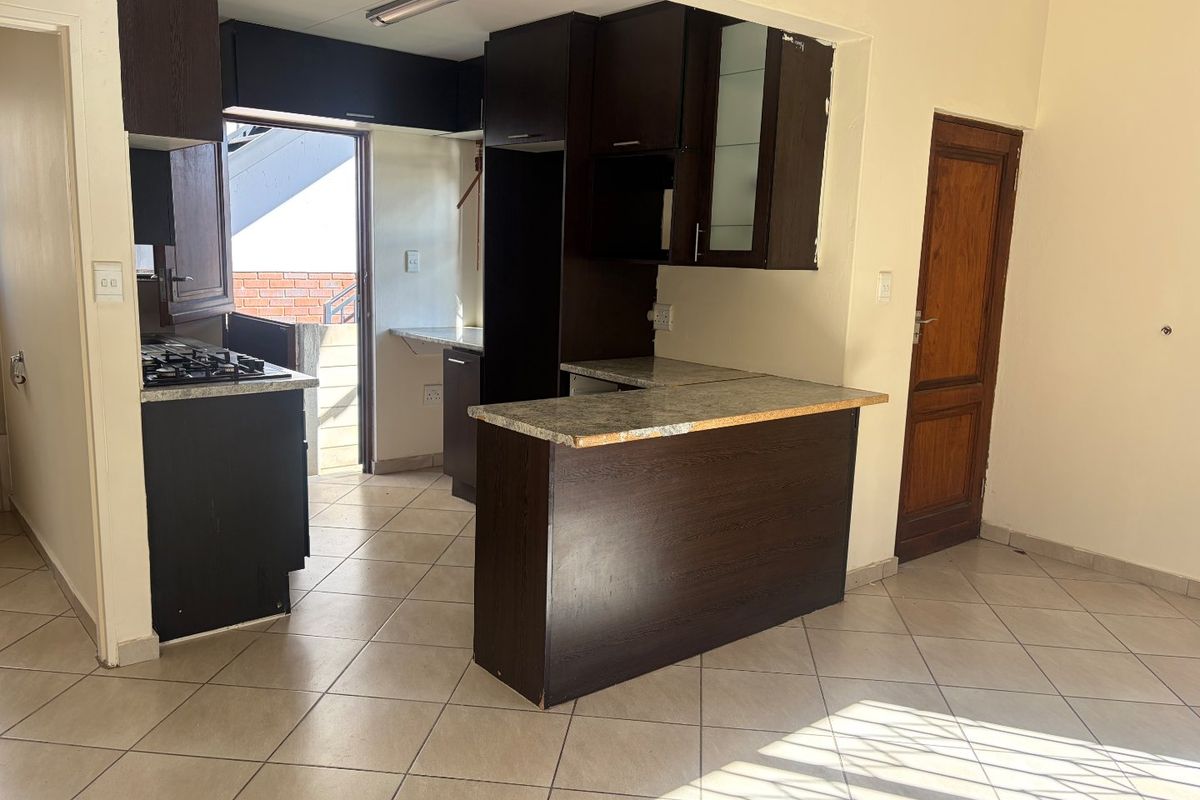 An empty kitchen featuring dark wood cabinetry, laminate countertops, a gas hob, and tiled flooring with direct access to an exterior area.