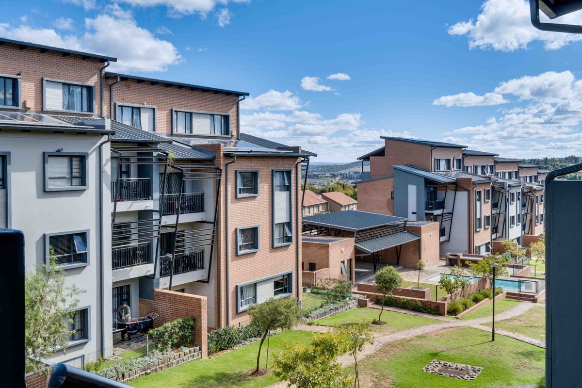 Elevated view of a modern apartment complex featuring brick facades, metal roofing, private balconies, a communal swimming pool, and well-maintained landscaped garden areas.