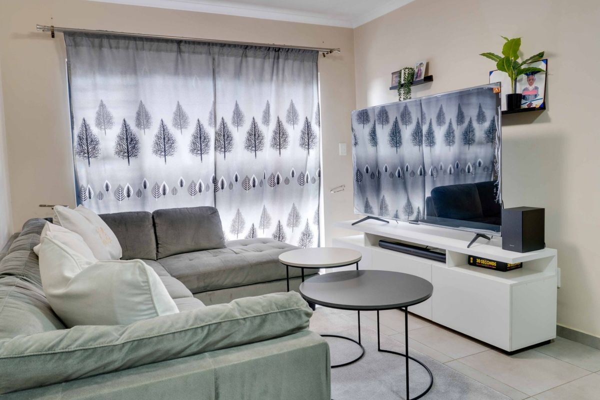 A comfortable living room featuring neutral tiled flooring and a large window dressed with patterned curtains, providing a bright and functional living space.
