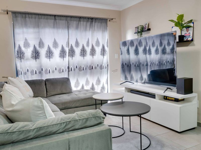 A comfortable living room featuring neutral tiled flooring and a large window dressed with patterned curtains, providing a bright and functional living space.