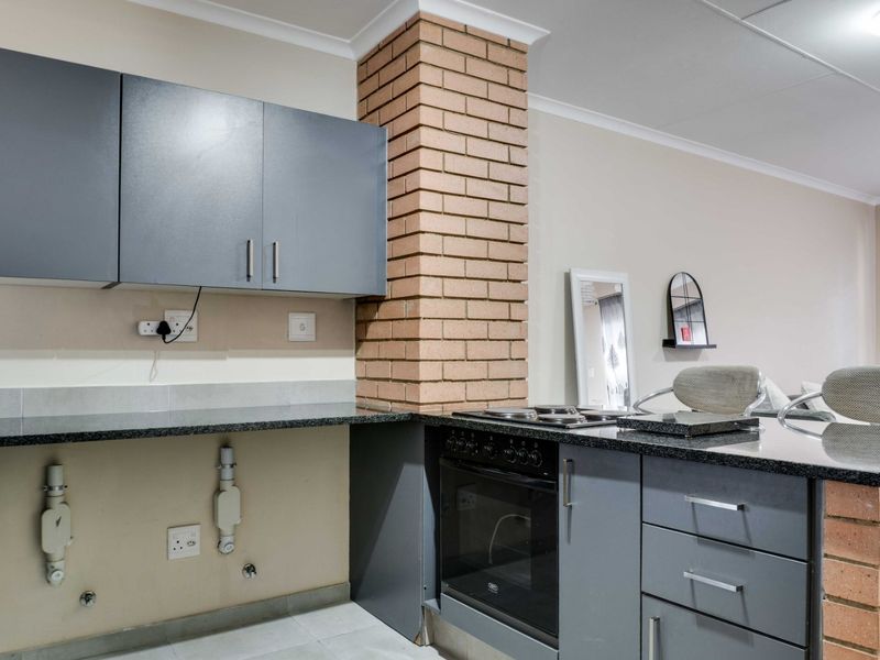 Kitchen area featuring grey cabinetry, granite countertops, a built-in oven with hob, and a distinctive exposed brick pillar.