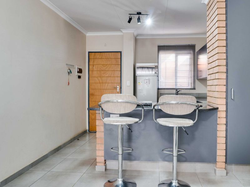 A functional kitchen area featuring a breakfast bar, exposed brick detailing, tiled flooring, and built-in cabinetry with modern track lighting.