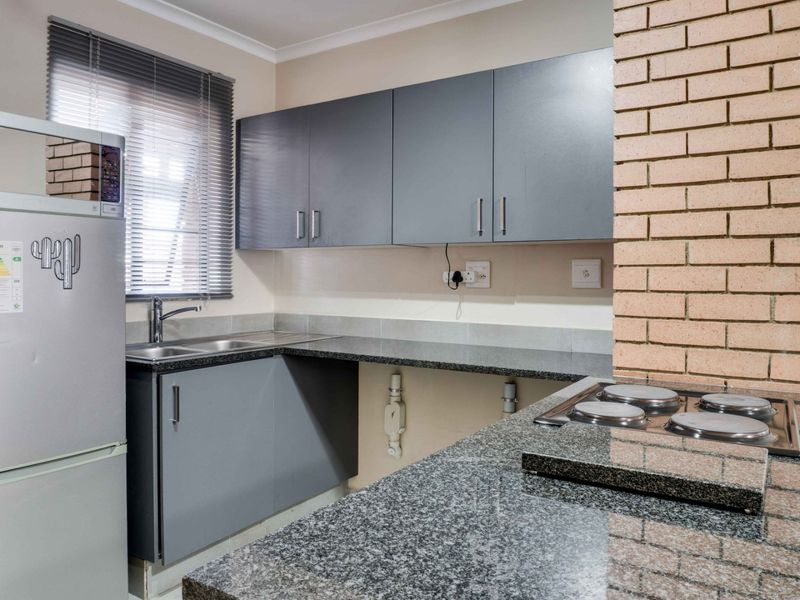Kitchen featuring grey cabinetry, granite countertops, a built-in hob, and an exposed brick feature wall, with some unfinished areas under the counter.