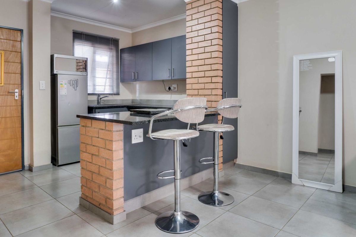 A functional kitchen featuring dark cabinetry, granite countertops, and a unique brick breakfast bar, complemented by neutral tiled flooring.