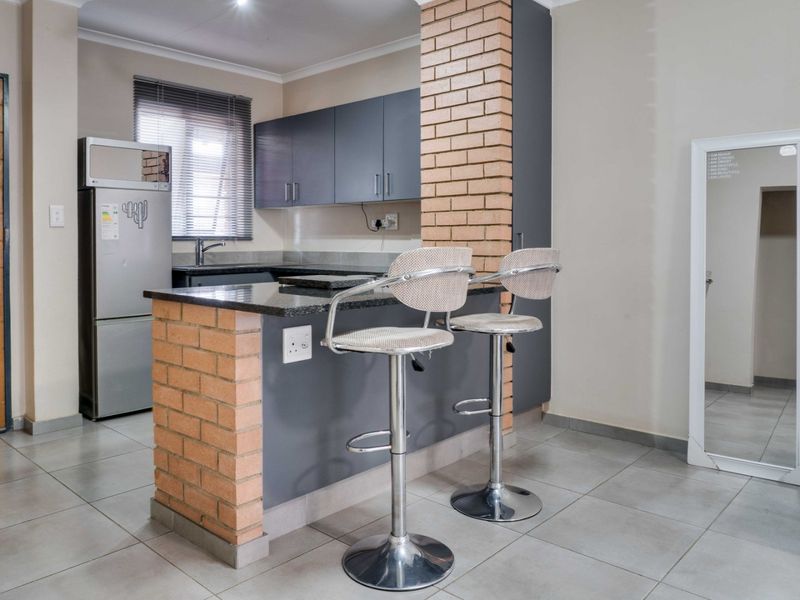 A functional kitchen featuring dark cabinetry, granite countertops, and a unique brick breakfast bar, complemented by neutral tiled flooring.