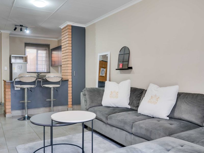 An open-plan living area featuring a breakfast bar with an exposed brick pillar, tiled flooring, and modern cabinetry, creating a functional and cohesive space.