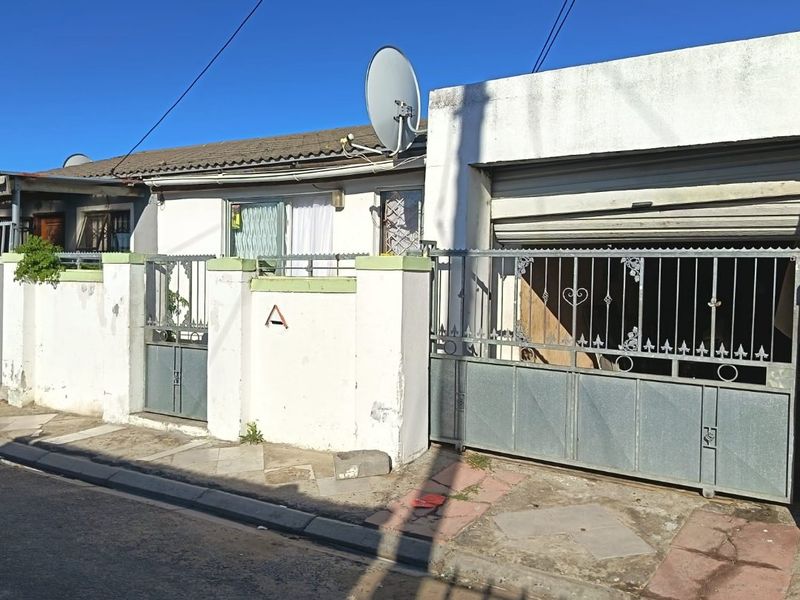 Front elevation of a single-story house featuring a metal security gate, boundary wall, and integrated garage access.