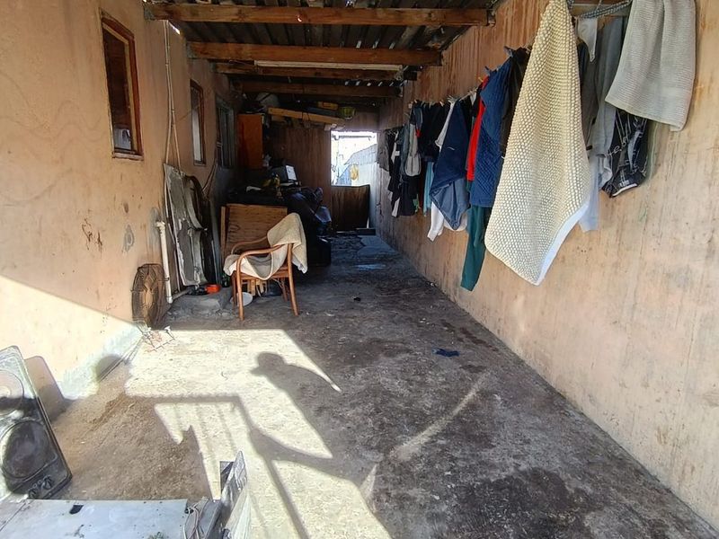 A utilitarian covered outdoor space featuring exposed timber rafters, corrugated roofing, and concrete flooring, currently used for storage and laundry drying.