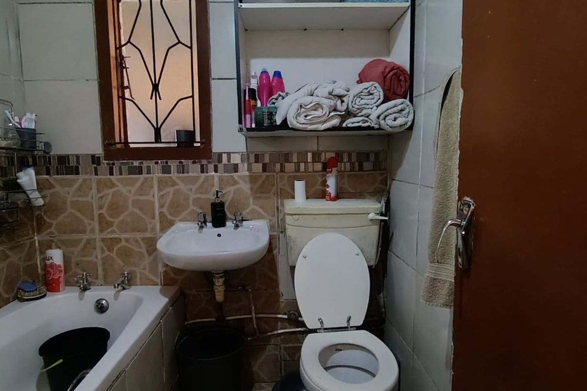 A compact bathroom featuring a bathtub, wall-mounted basin, and toilet with tiled finishes and built-in shelving.