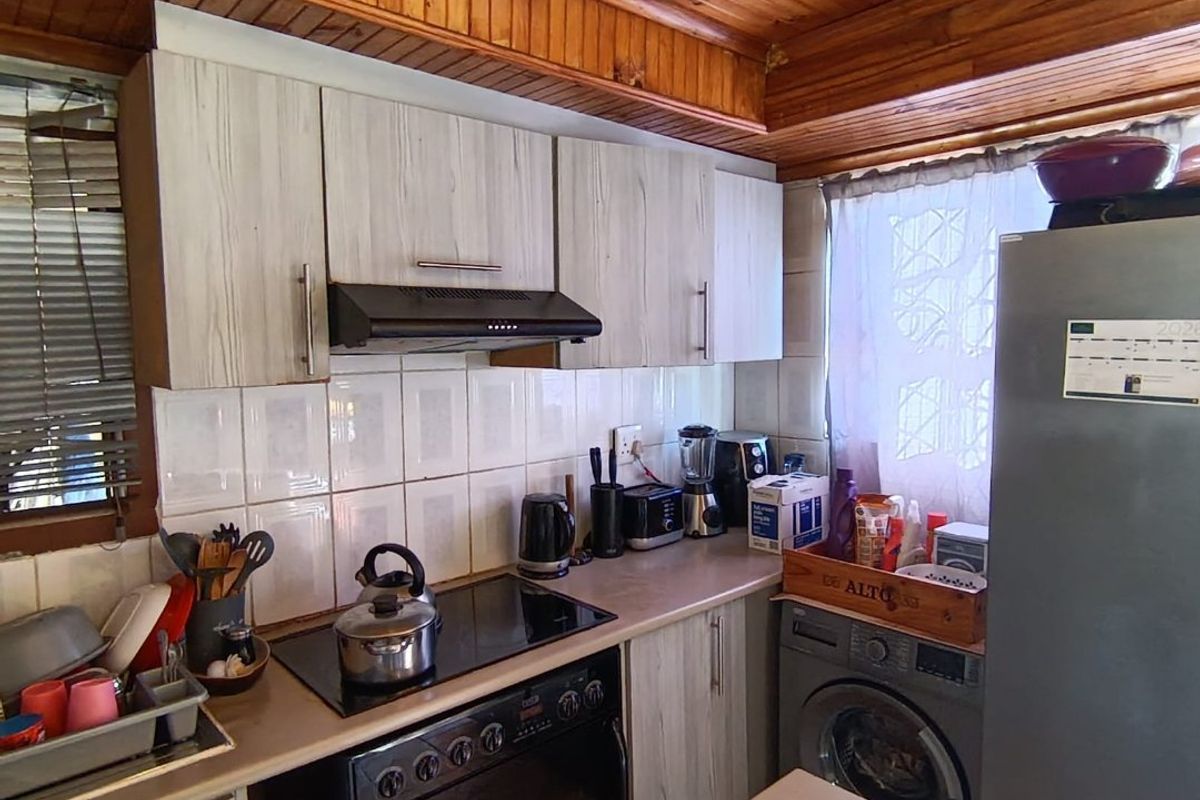 Compact kitchen featuring light-toned cabinetry, laminate countertops, a built-in electric stove with extractor, and a distinctive timber-clad ceiling.