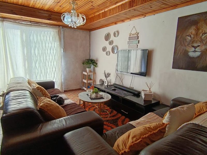 A living room featuring a distinctive timber tongue and groove ceiling, a crystal chandelier, and a security gate over the window.