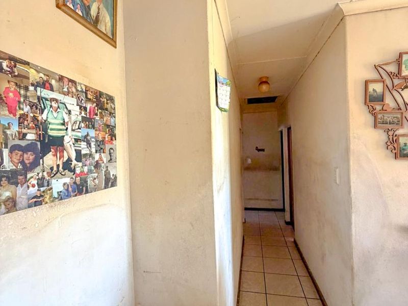 A narrow interior hallway featuring tiled flooring and standard ceiling finishes, currently showing signs of wear and requiring cosmetic updates to the wall surfaces.