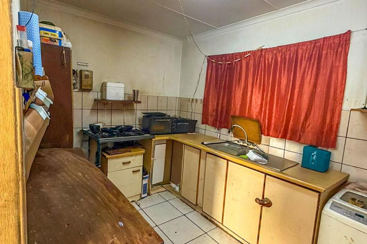 A dated kitchen featuring original cabinetry, tiled flooring, and a stainless steel sink, requiring significant renovation and modernization to improve functionality and aesthetic appeal.