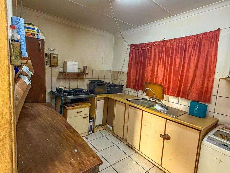 A dated kitchen featuring original cabinetry, tiled flooring, and a stainless steel sink, requiring significant renovation and modernization to improve functionality and aesthetic appeal.