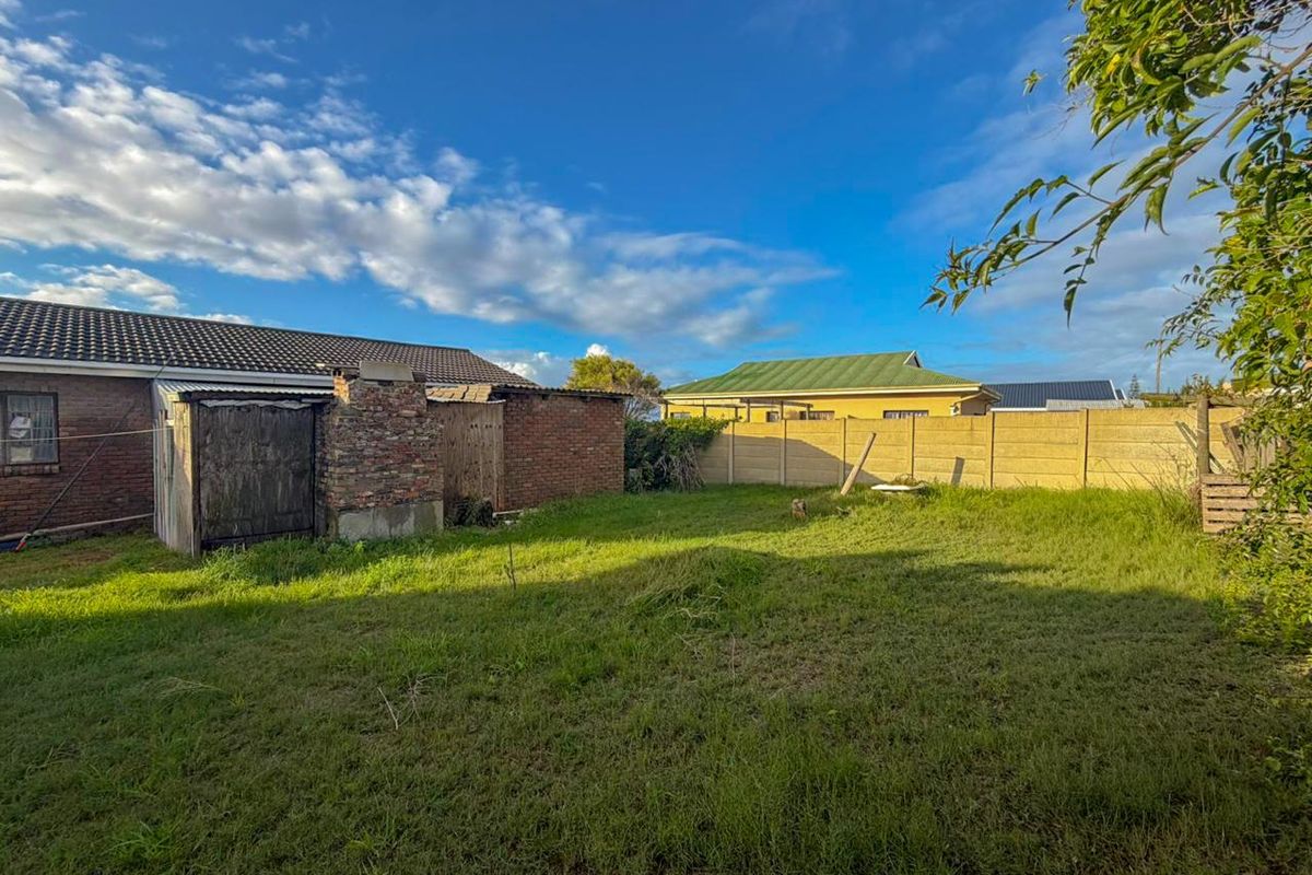 Rear garden area featuring a lawn, precast boundary walling, and an existing brick outbuilding with an external chimney structure.