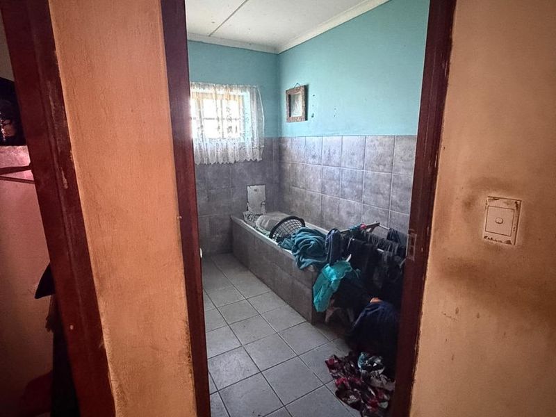 A functional bathroom featuring tiled flooring and wall cladding with a built-in bathtub, requiring cosmetic updates to improve its overall condition.