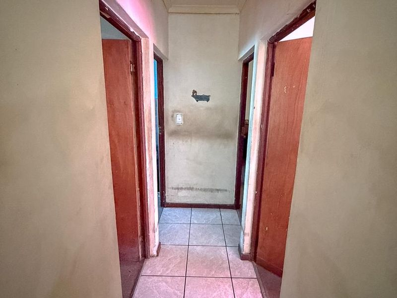 A narrow hallway featuring tiled flooring and multiple timber doors, showing significant signs of wear and wall staining requiring maintenance.