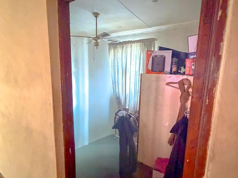 A bedroom interior viewed through a doorway, featuring a ceiling fan and showing signs of wear on the walls and door frame.