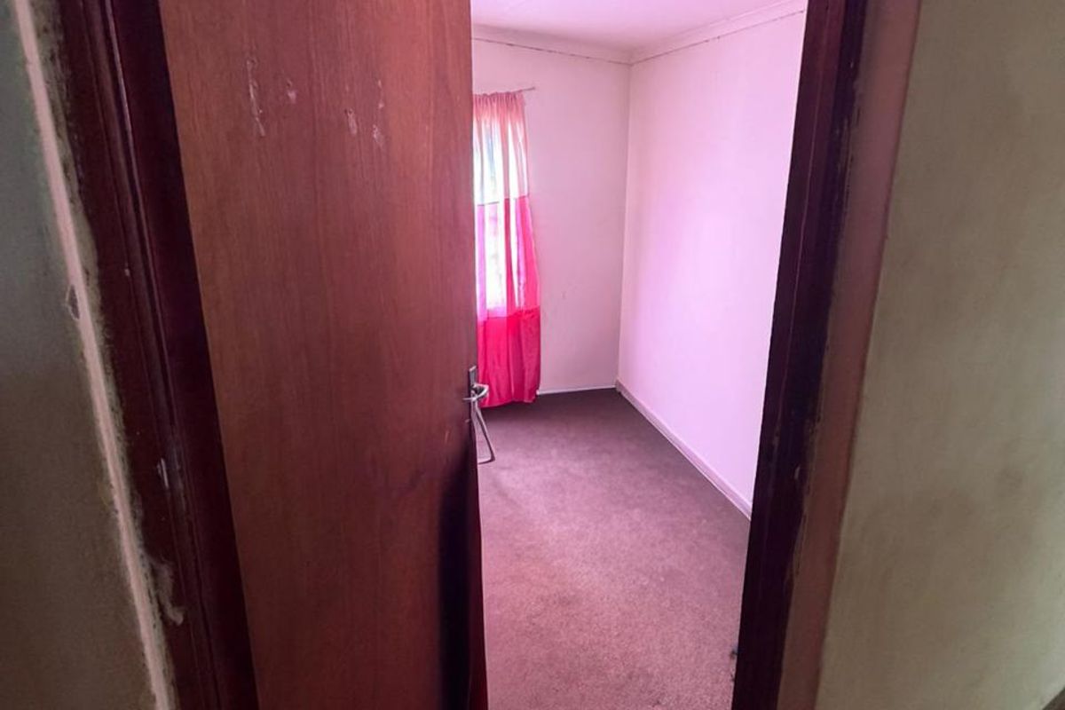 An empty bedroom featuring carpet flooring and a ceiling light fixture, showing signs of wear and ceiling damage.