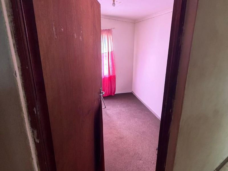 An empty bedroom featuring carpet flooring and a ceiling light fixture, showing signs of wear and ceiling damage.