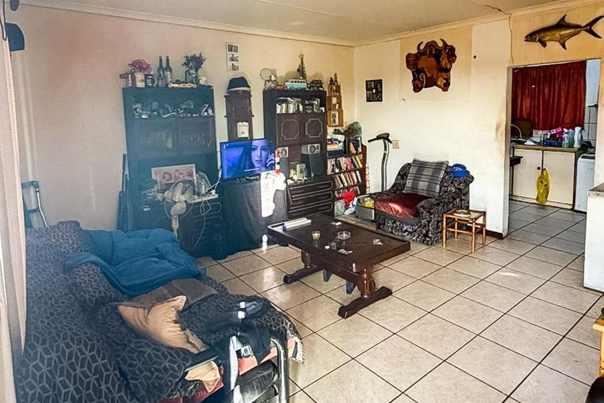 A living room area featuring tiled flooring and ceiling tiles, showing signs of wear and requiring cosmetic updates to improve the overall aesthetic.