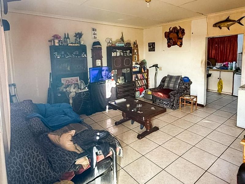A living room area featuring tiled flooring and ceiling tiles, showing signs of wear and requiring cosmetic updates to improve the overall aesthetic.