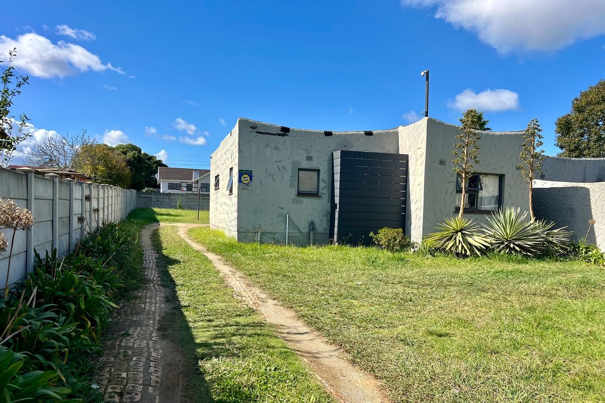 Rear view of the property featuring a textured exterior finish, a paved pathway, and a precast concrete boundary wall set within a grassed yard.