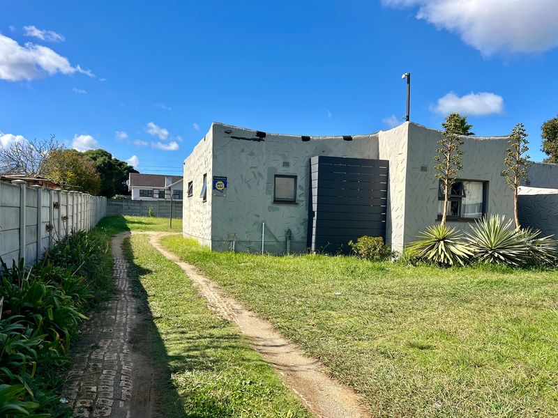 Rear view of the property featuring a textured exterior finish, a paved pathway, and a precast concrete boundary wall set within a grassed yard.
