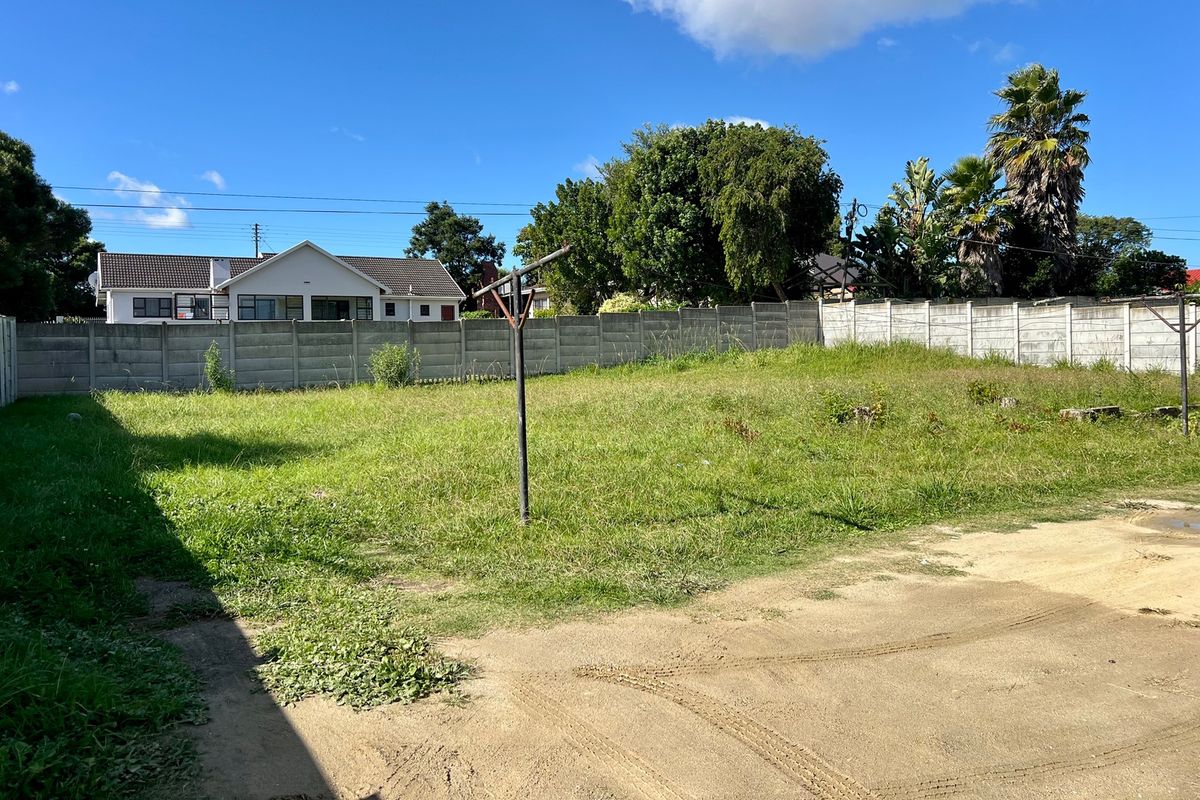 A vacant residential plot featuring a large grassed area, enclosed by a precast concrete boundary wall with a rotary clothesline installed.