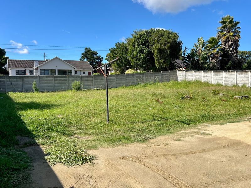 A vacant residential plot featuring a large grassed area, enclosed by a precast concrete boundary wall with a rotary clothesline installed.