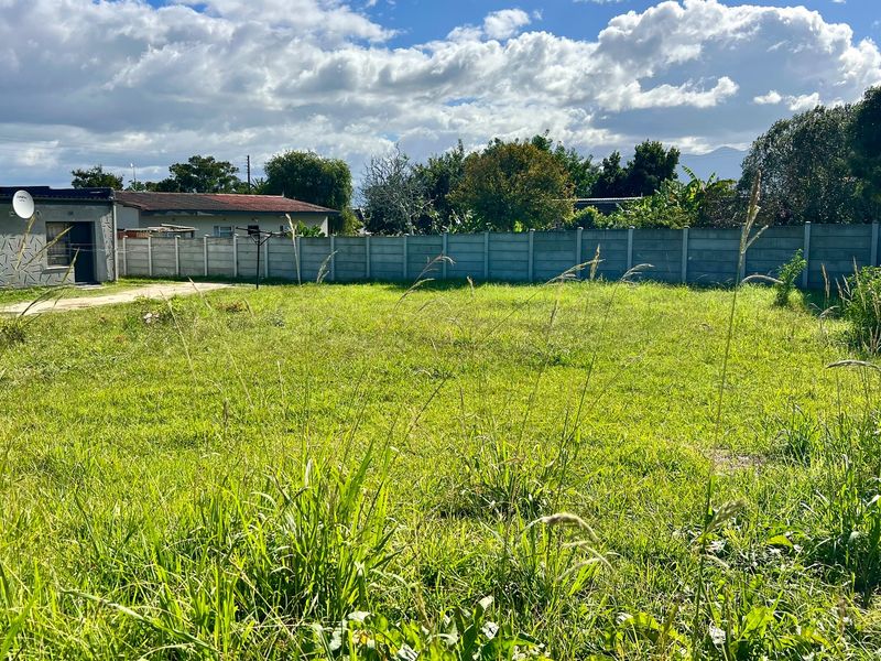A vacant residential plot featuring a grass lawn and enclosed by a precast concrete boundary wall.