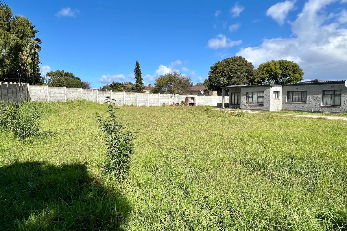 A spacious rear yard featuring a large lawn, a precast concrete boundary wall, and a built-in brick braai area.