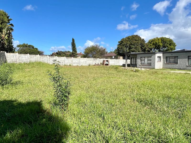 A spacious rear yard featuring a large lawn, a precast concrete boundary wall, and a built-in brick braai area.
