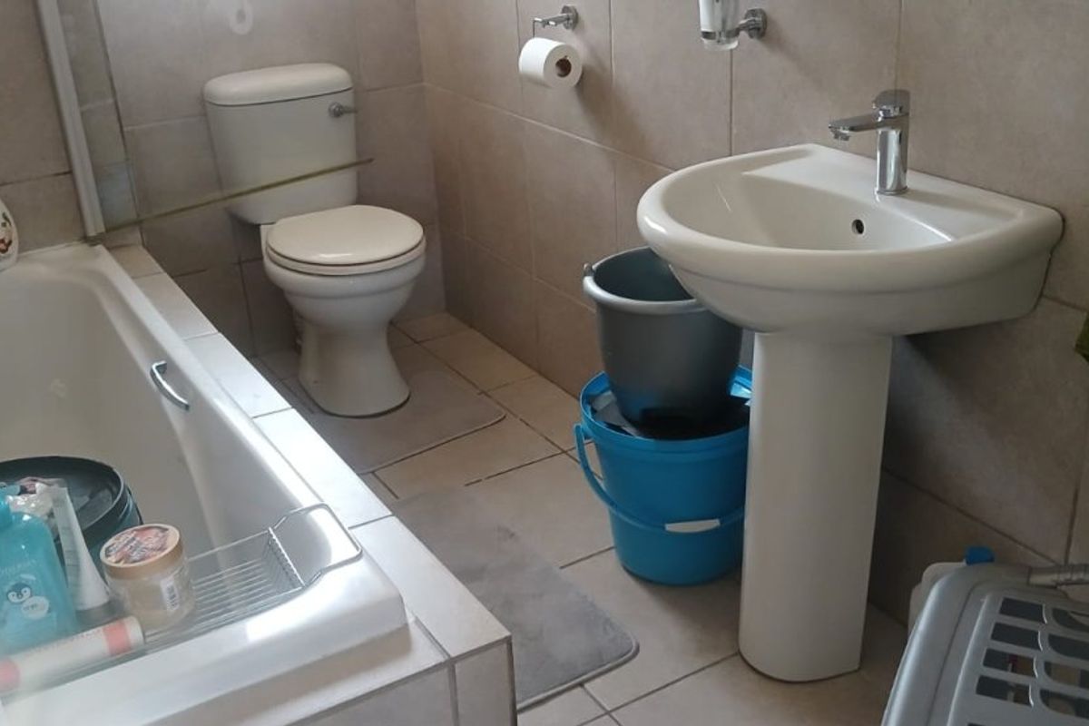 A functional bathroom featuring a pedestal basin, bathtub, and toilet with neutral wall and floor tiling.