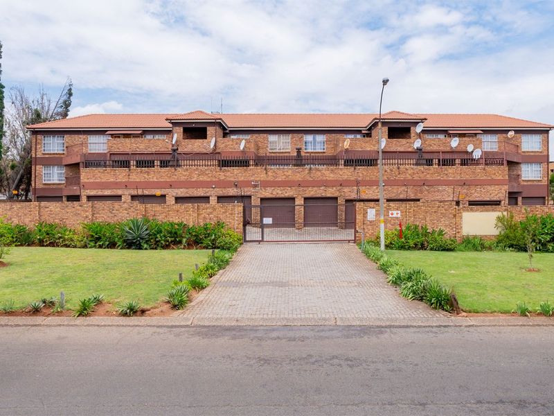 Front view of a multi-story facebrick apartment complex featuring a paved driveway, secure gated entrance, and private balconies.